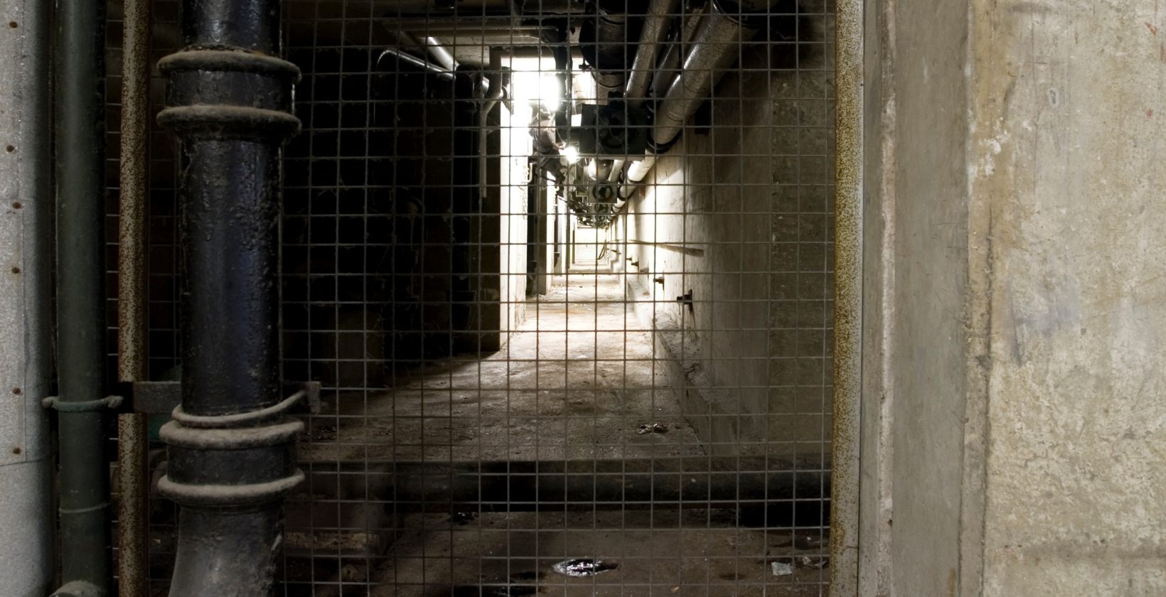 Basement gas pipework in London buildings Below ground service corridor carrying pipework behind a mesh gate, typical of the basements where London gas supplies run