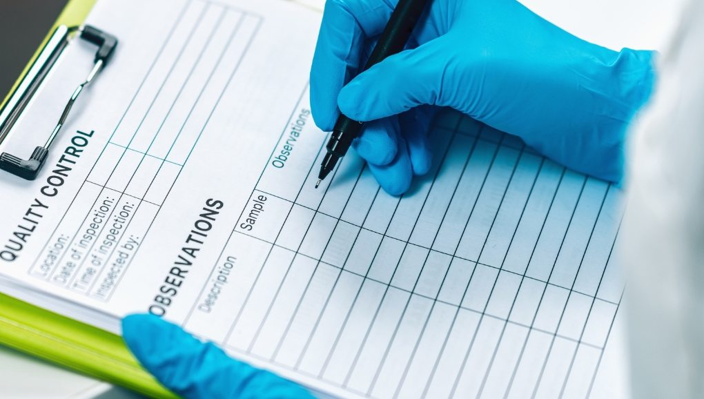 Inspector in blue gloves completing an inspection record on a clipboard