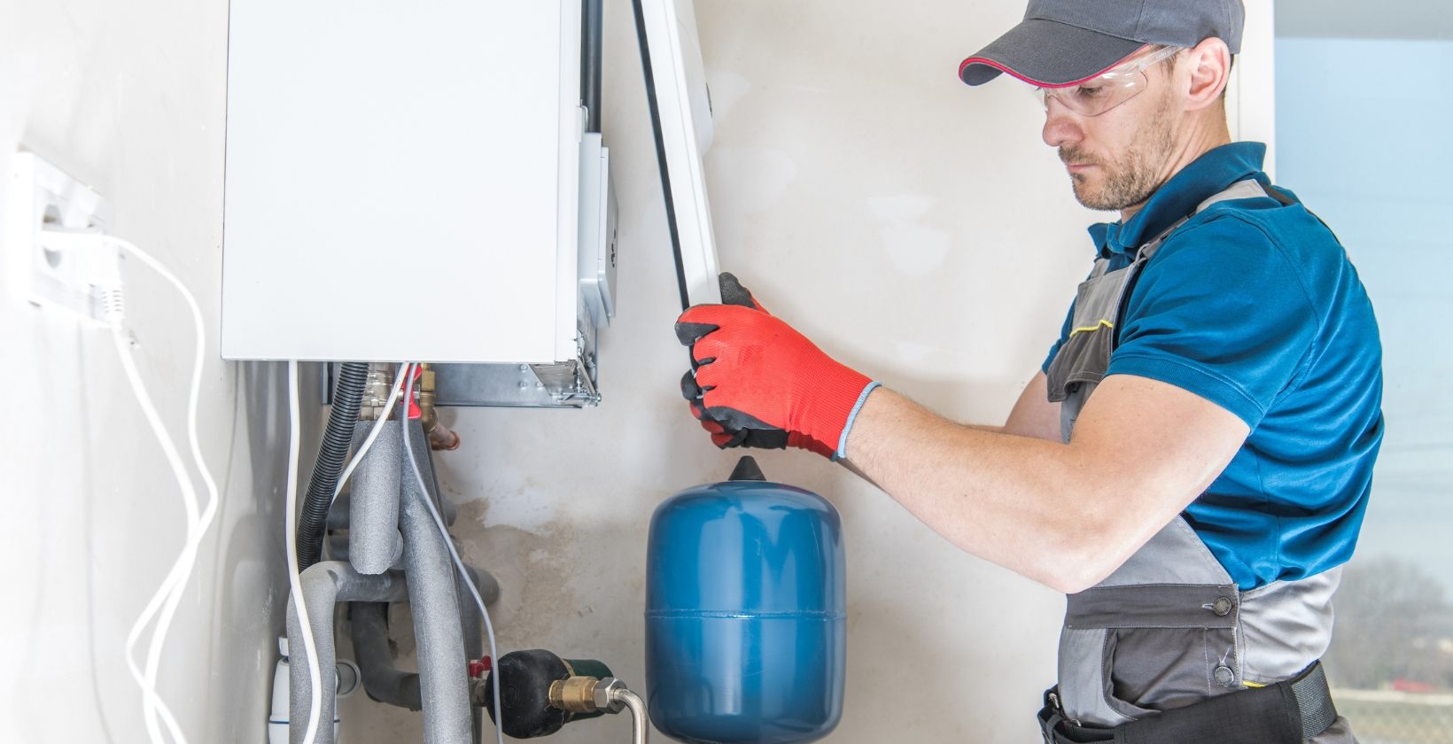 Gas engineer in safety glasses and gloves fitting the casing of a commercial boiler