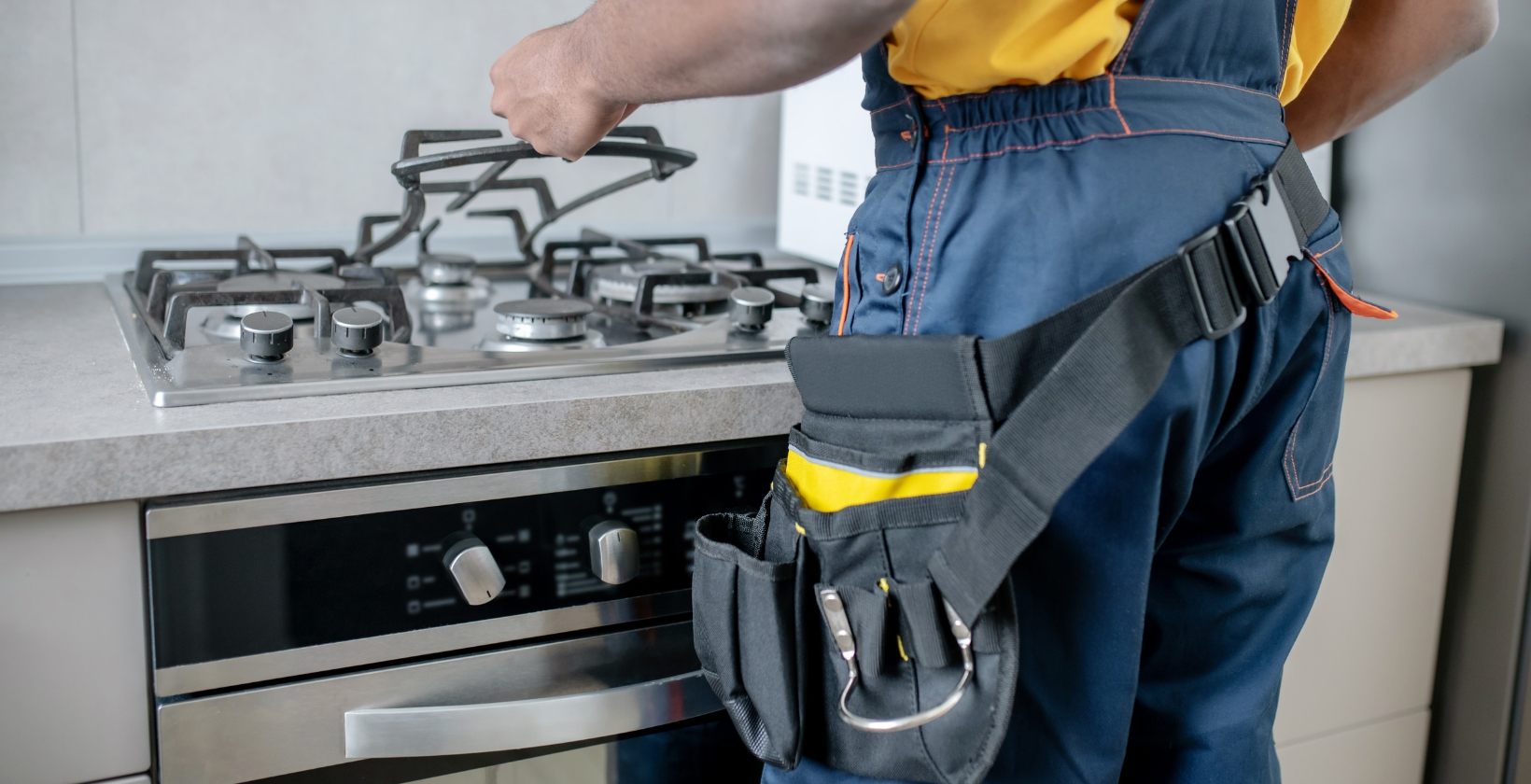 Engineer wearing a tool belt lifting the pan support from a gas hob during a repair