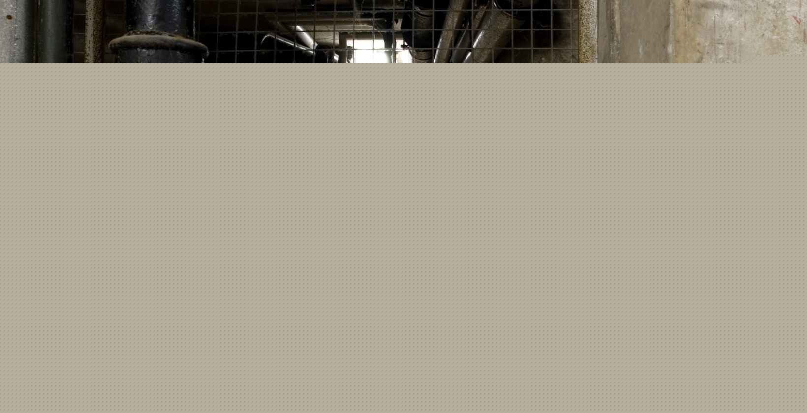 Below-ground service corridor carrying gas and utility pipework behind a mesh safety gate